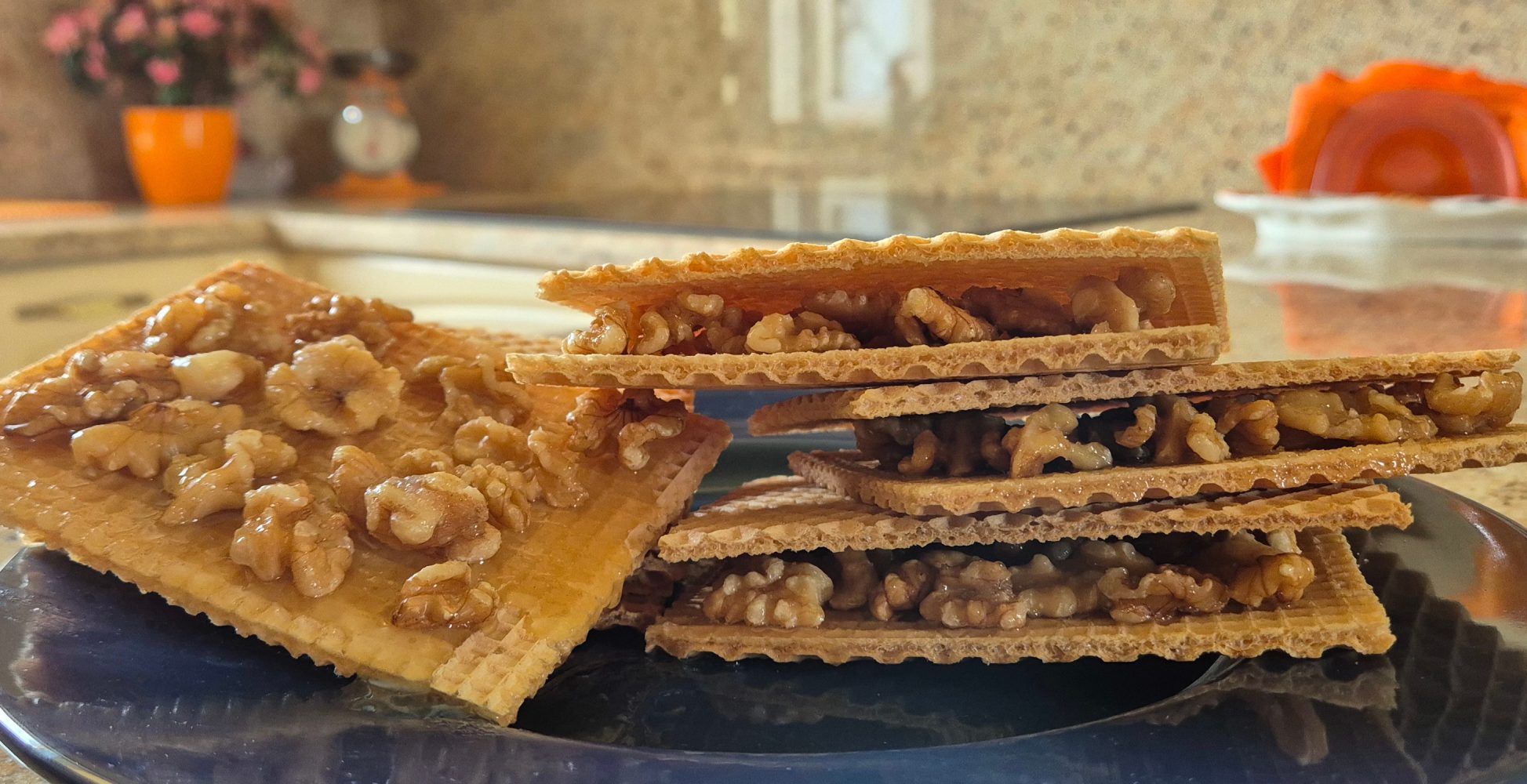 Cialde croccanti rettangolari farcite con gherigli di noce e miele, impilate su un piatto scuro in un ambiente domestico luminoso - Rectangular crispy wafers filled with walnut kernels and honey, stacked on a dark plate in a bright home setting