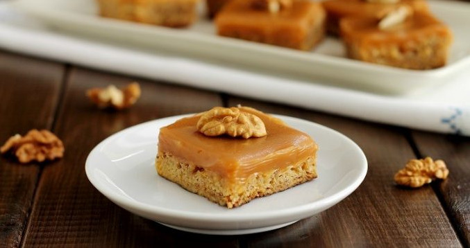 Un brownie quadrato al cioccolato bianco guarnito con glassa al caramello e mezza noce, servito su un piattino bianco - A square white chocolate brownie topped with caramel glaze and half a walnut, served on a white saucer