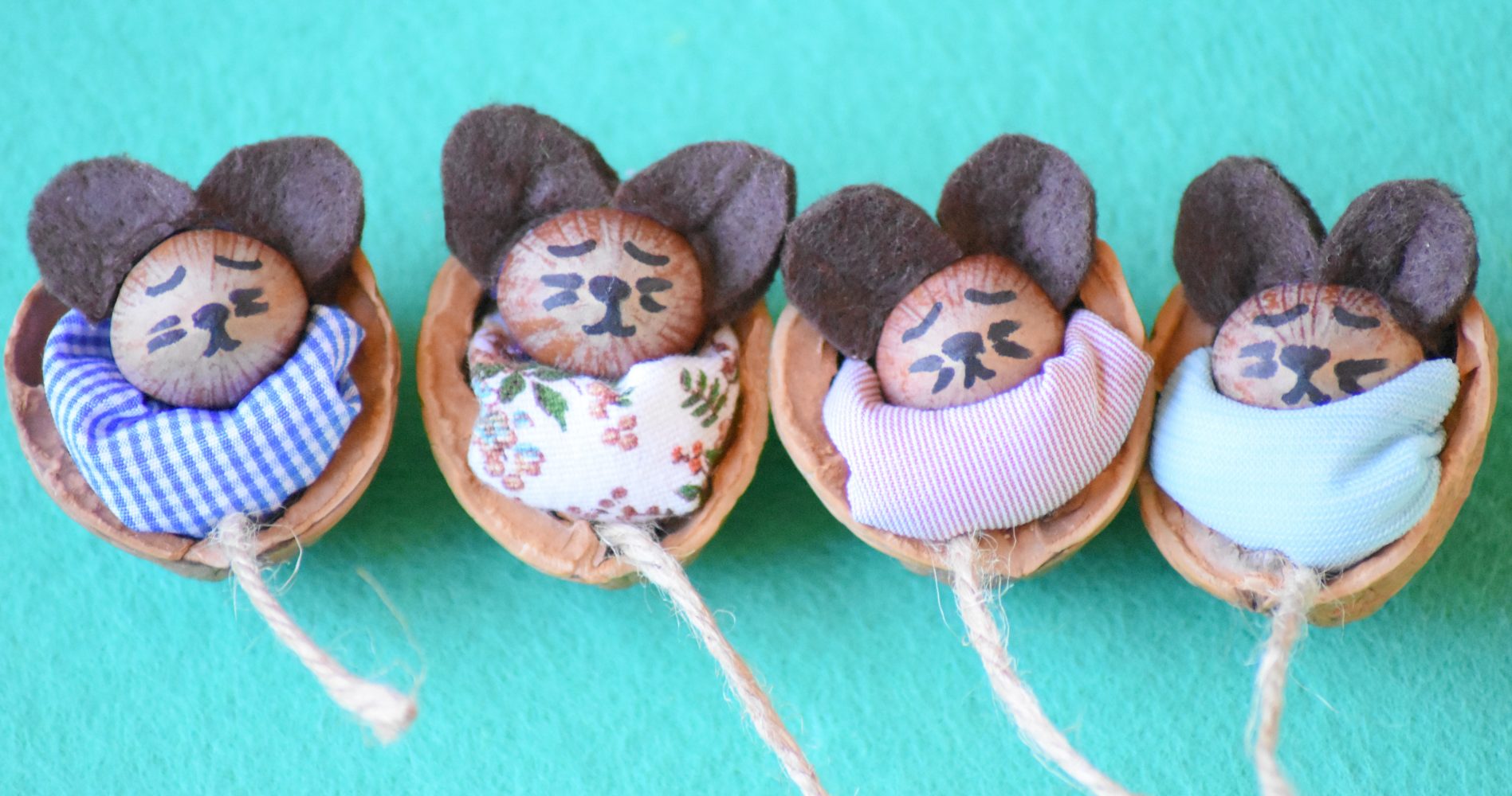 Quattro topi artigianali, realizzati con gusci di noce, panno e scampoli di stoffa, allineati su uno sfondo verde acqua - Four handmade mice made from walnut shells, cloth, and fabric scraps, lined up on a teal background