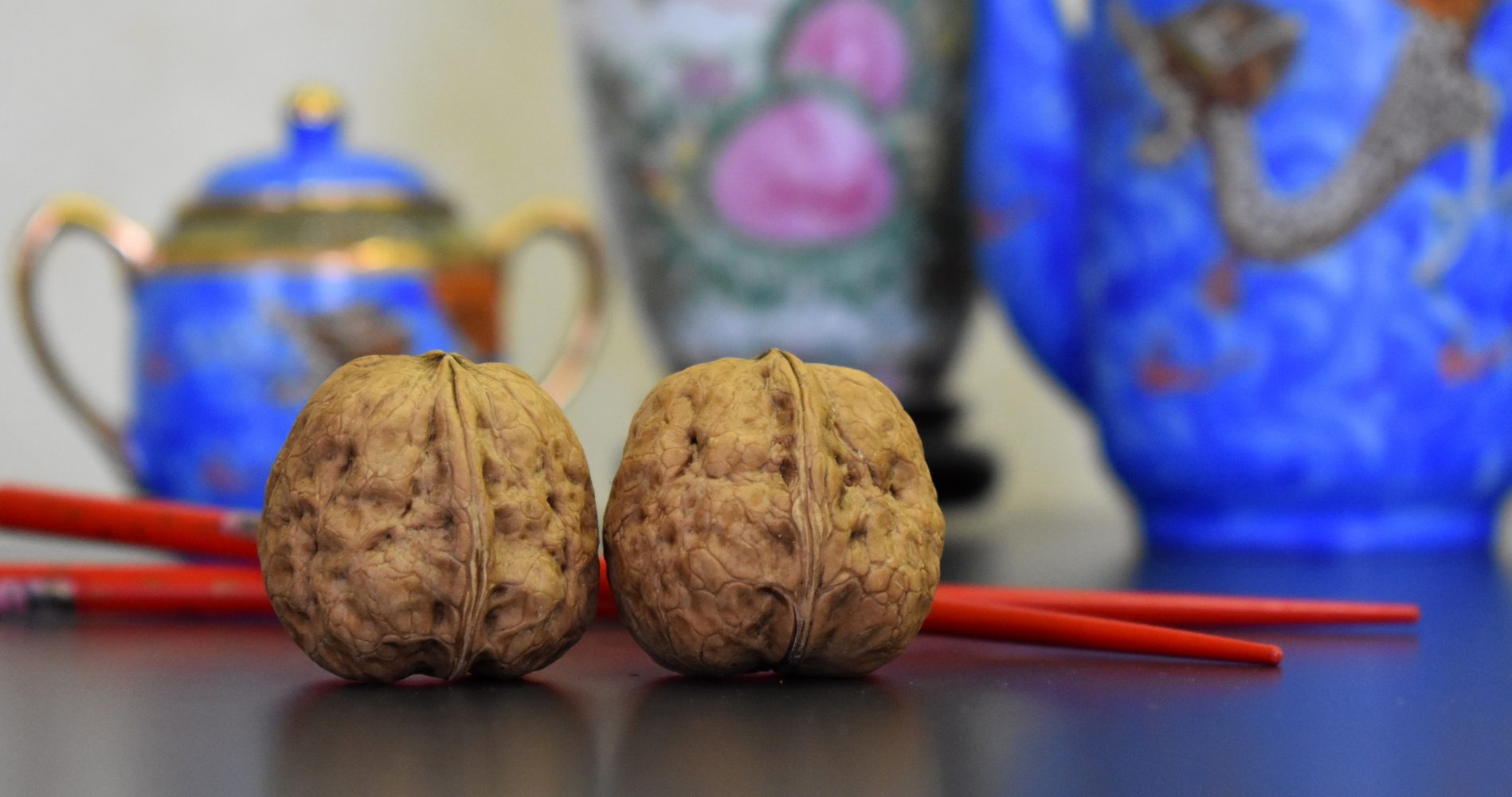 Primo piano di due noci con guscio e bacchette rosse, davanti a ceramiche cinesi decorative | Close-up of two walnuts in their shells with red chopsticks, in front of decorative Chinese ceramics