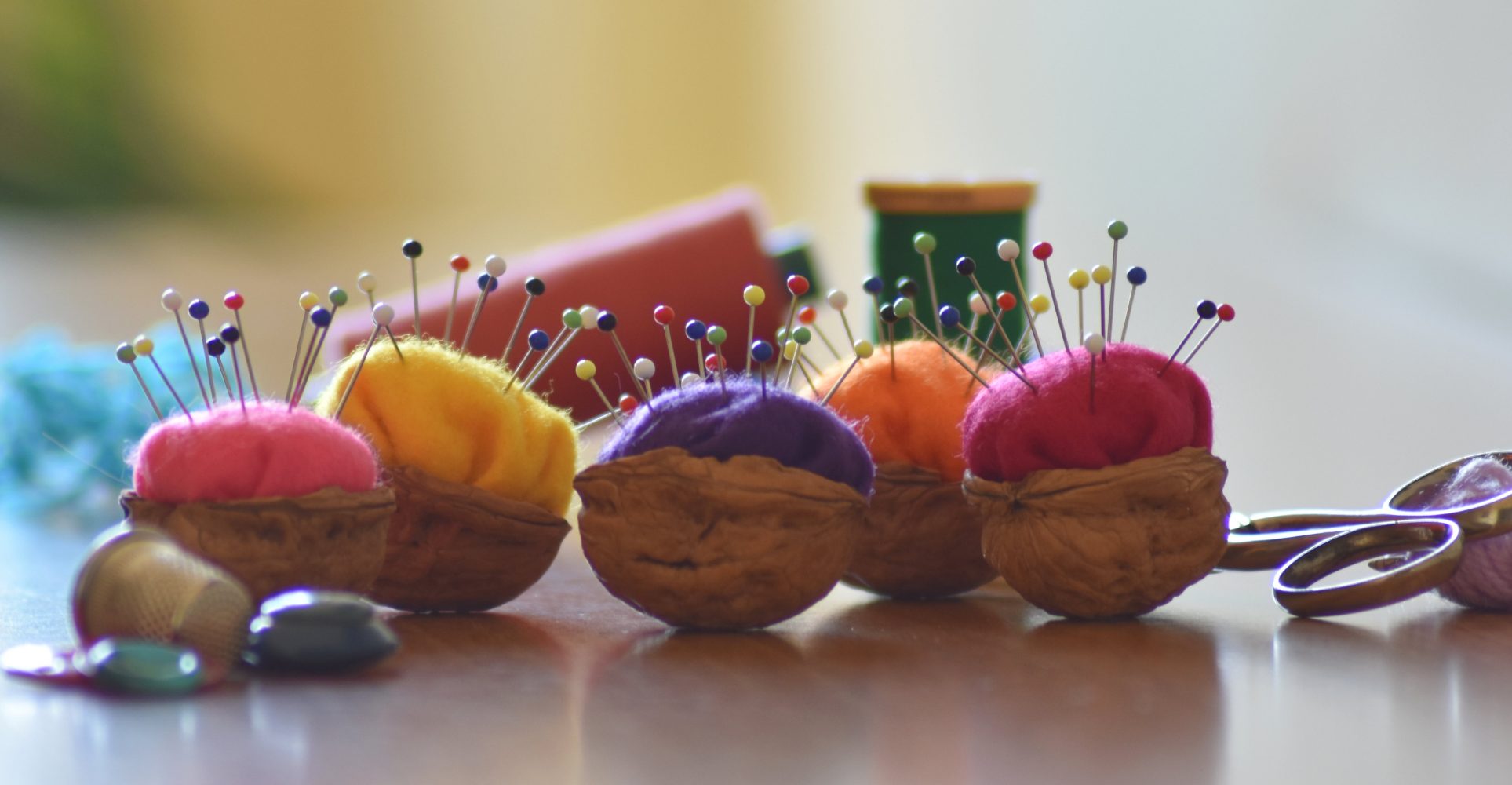 Quattro gusci di noce trasformati in puntaspilli colorati, allineati su un tavolo di legno - Four walnut shells turned into colorful pincushions, lined up on a wooden table