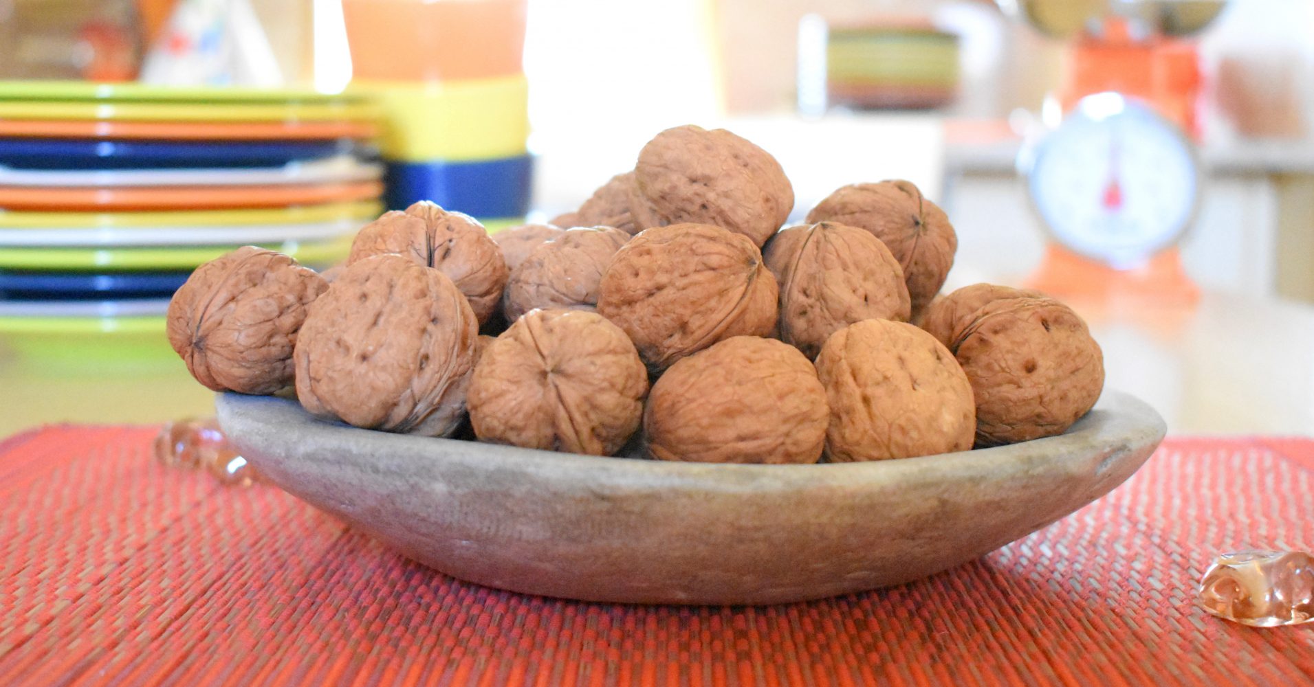 Una ciotola di pietra rustica colma di noci intere con il guscio, posizionata su una tovaglietta rossa - A rustic stone bowl filled with whole walnuts in their shells, placed on a red placemat