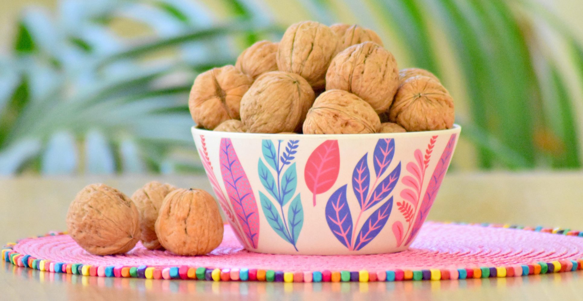 Ciotola decorata piena di noci nel guscio su un tappetino rosa vivace - Decorated bowl filled with whole walnuts in their shells on a bright pink mat.