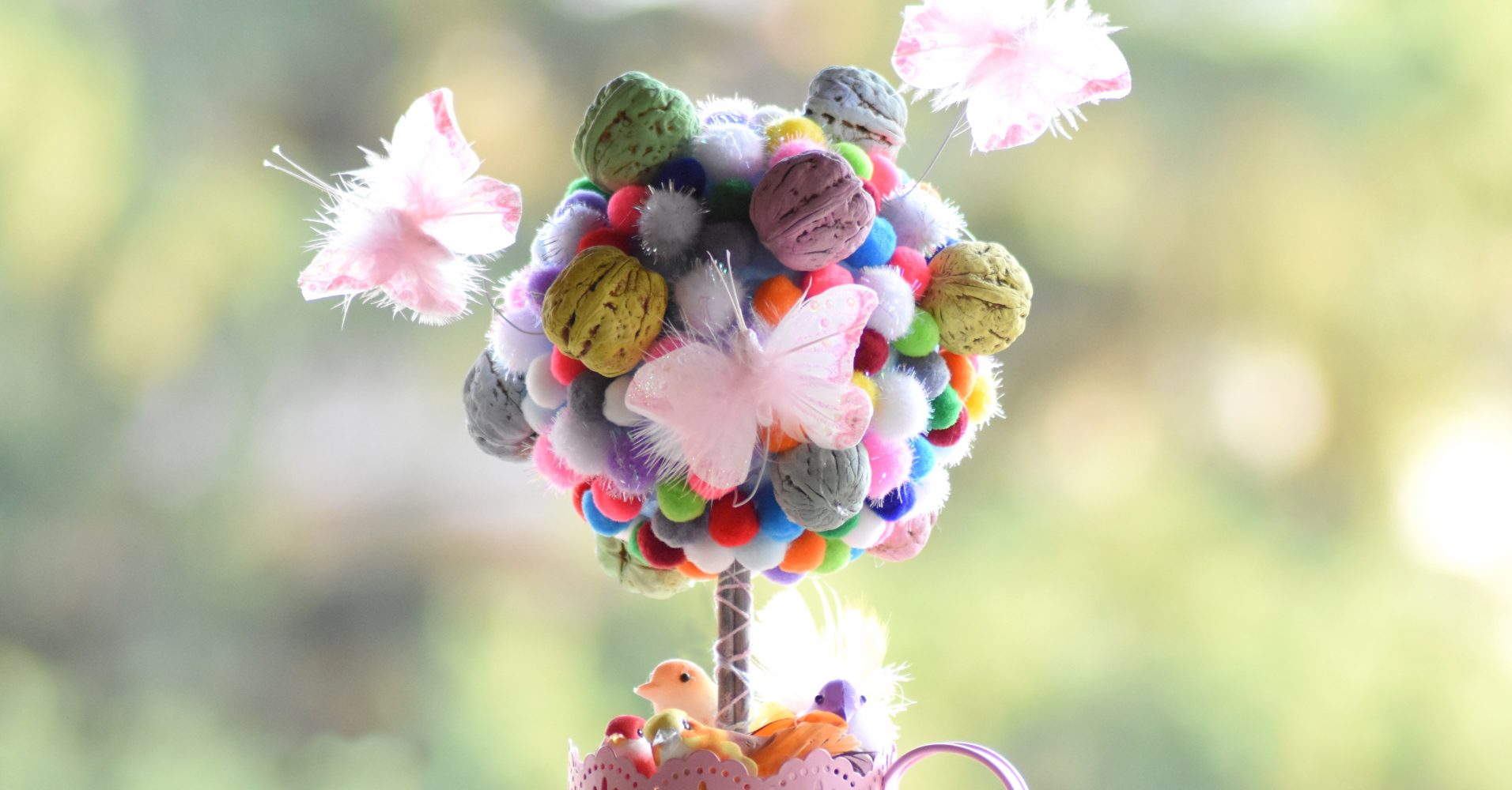 Centrotavola creativo a forma di alberello composto da pompon colorati e gusci di noce dipinti - Creative table centerpiece shaped like a small tree, made of colorful pom-poms and painted walnut shells