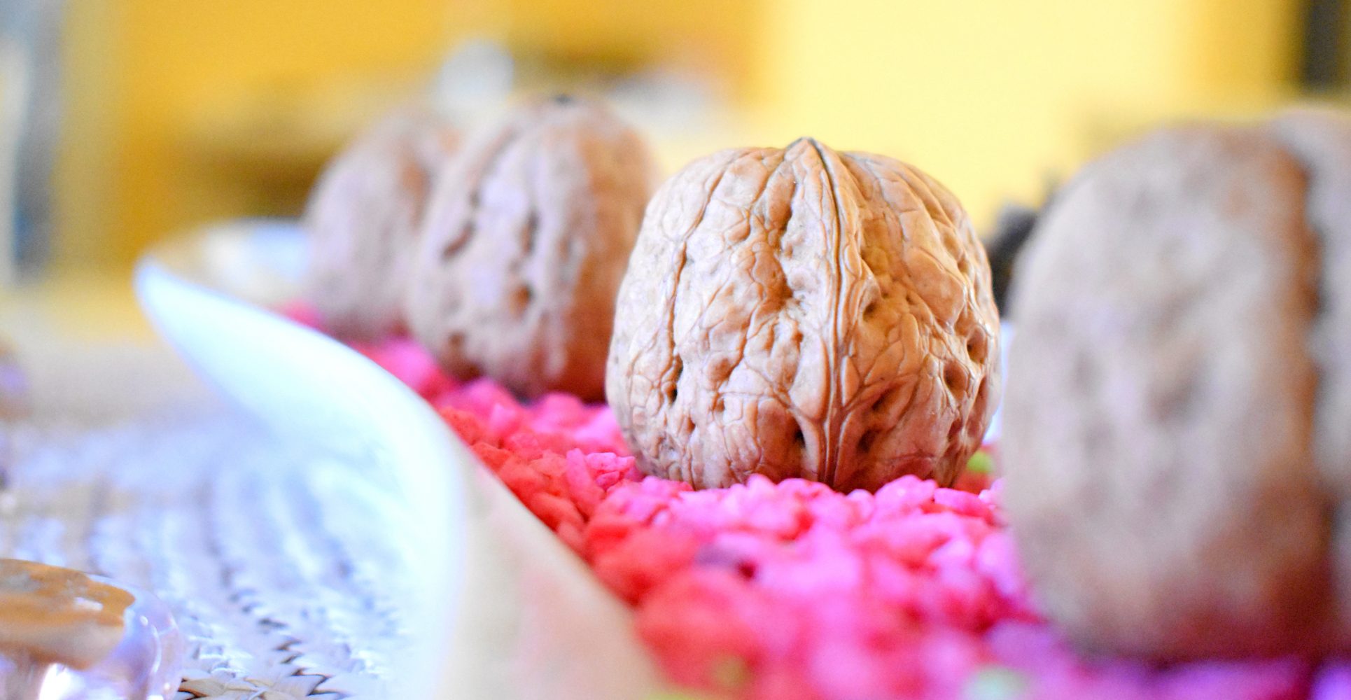 Primo piano ravvicinato di una fila di noci intere adagiate su un letto di graniglia rosa vivace all'interno di un vassoio bianco - Close-up of a row of whole walnuts resting on a bed of bright pink gravel inside a white tray
