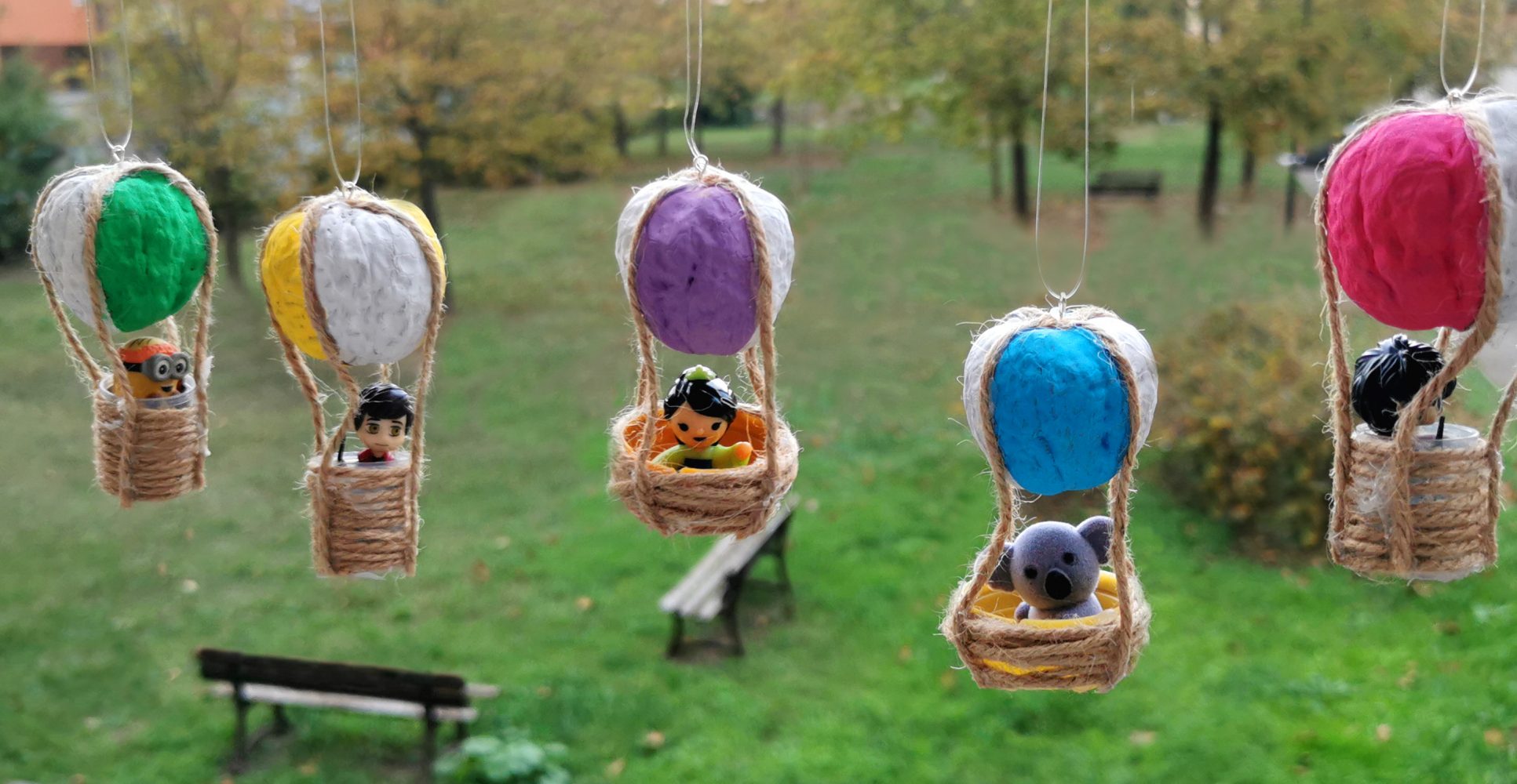 Lavoretto creativo per bambini: mongolfiere fatte a mano con gusci di noce colorati, spago e piccole miniature, appese con uno sfondo di un parco verde sfocato - Creative children’s craft: handmade hot air balloons made from painted walnut shells, string, and small miniature figures, hanging against a blurred green park background