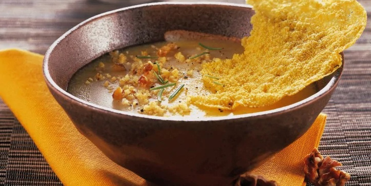 Una ciotola di crema di polenta guarnita con granella di noci e rosmarino, accompagnata da una cialda di formaggio croccante - A bowl of creamy polenta topped with chopped walnuts and rosemary, accompanied by a crispy cheese wafer