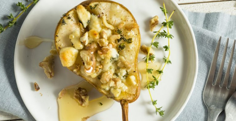 Mezza pera al forno farcita con formaggio gorgonzola e noci su un piatto bianco - Half a baked pear stuffed with gorgonzola cheese and walnuts, served on a white plate