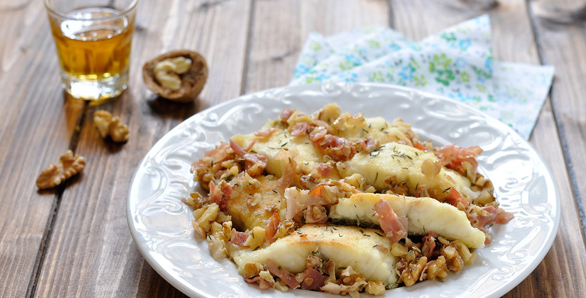 Filetti di pesce bianco cotti in padella e guarniti con speck croccante e noci tritate, serviti su un piatto bianco decorato - White fish fillets pan-seared and garnished with crispy speck and chopped walnuts, served on a white plate