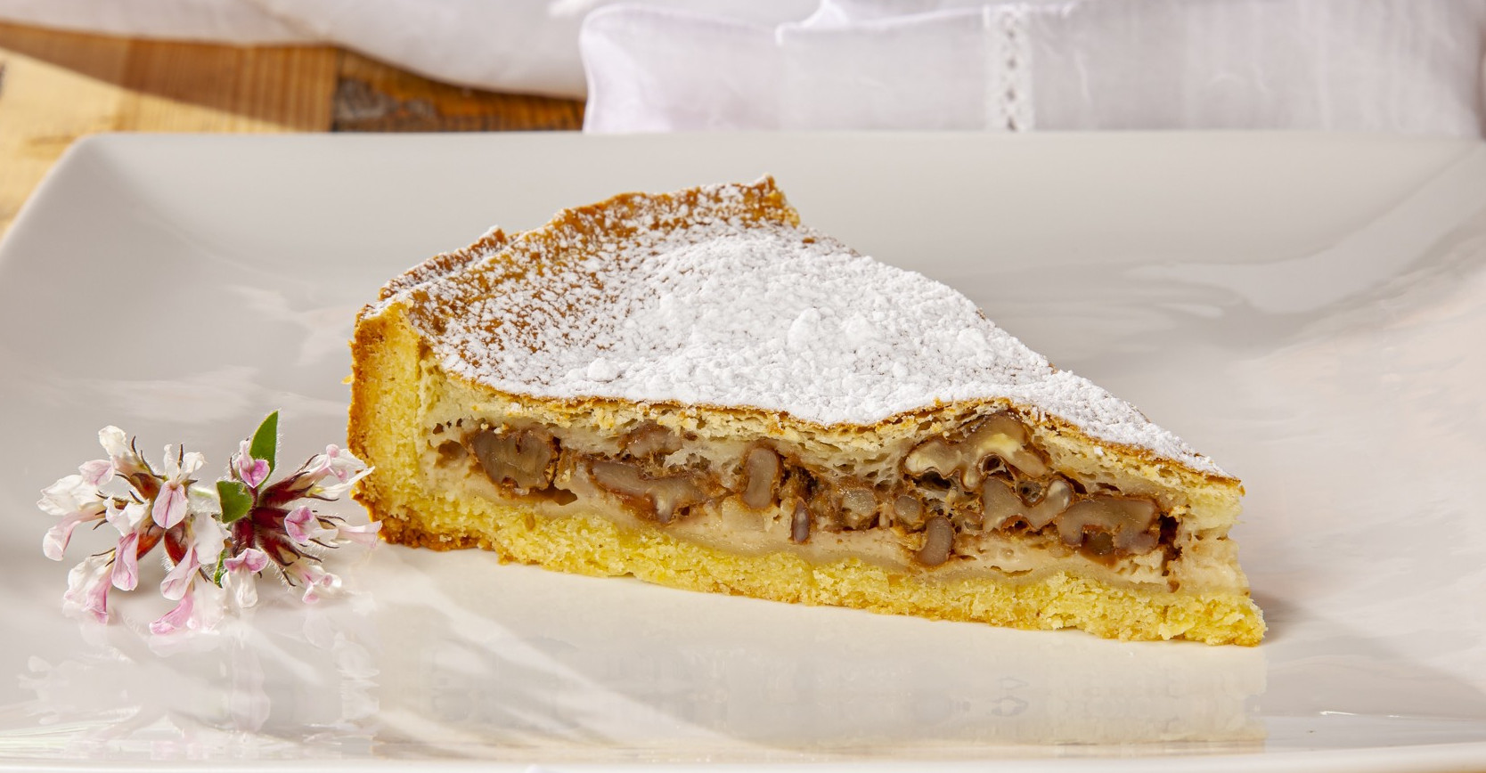 Fetta di crostata alle noci con zucchero a velo su un piatto bianco - A slice of walnut tart dusted with powdered sugar on a white plate